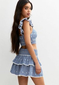 Conjunto de dos piezas a cuadros en azul y blanco que presenta un top cropped con volantes y una falda de capas con borde de encaje y cinturilla fruncida.