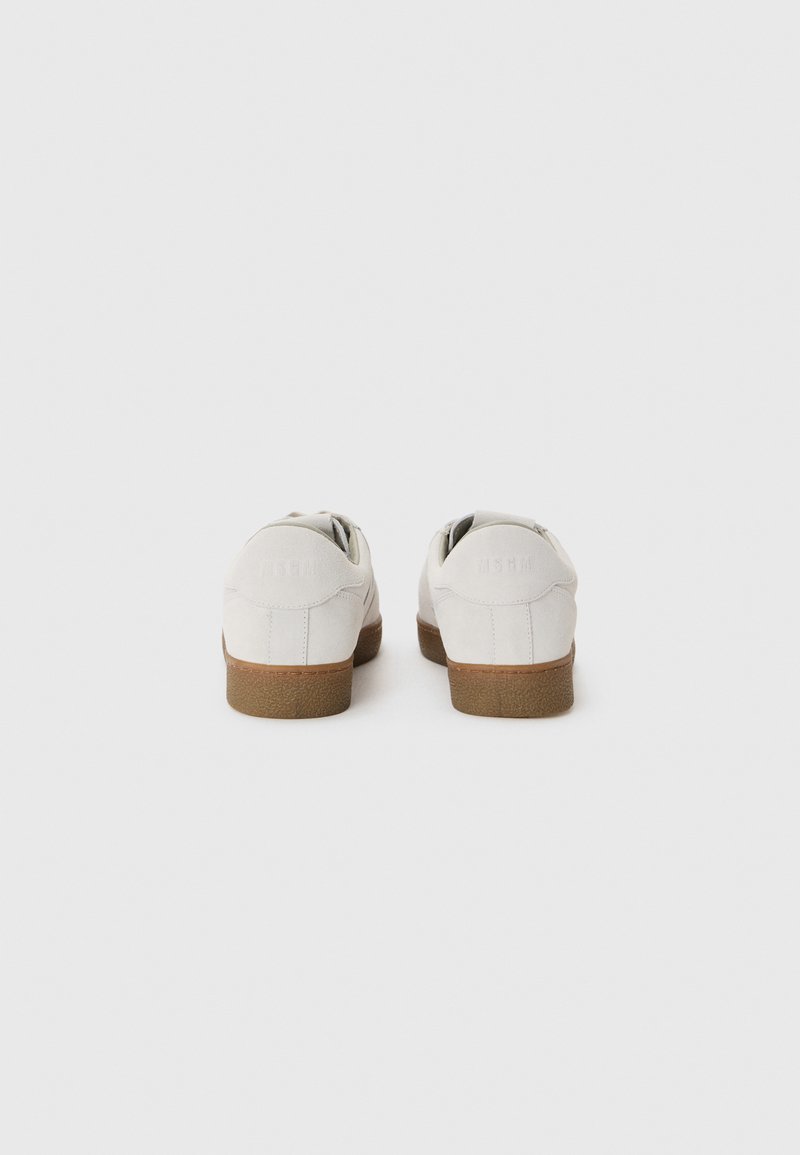 Baskets en suède blanc avec une semelle en caoutchouc brun texturé, présentant des arrière arrondis et un design minimaliste. Aucun logo ou motif visible.