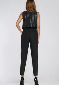 Czarny top bez rękawów z cekinami, połączony z dopasowanymi czarnymi spodniami i wysokimi obcasami. Zestaw zawiera marszczoną talię i dopasowany krój.