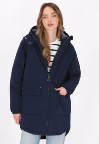 Tamnoplavi parka kaput s kapuljačom, prednjim zatvaračem, elastičnim manžetama i dva prednja džepa. Podstavljen sivoj flisom. Nosiv preko prugaste bluze.