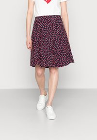Gonna blu con una forma svasata, caratterizzata da un motivo ripetuto di piccoli cuori rossi, realizzata in tessuto leggero. Indossata con sneakers bianche.