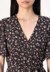 Robe portefeuille noire à fleurs avec des manches courtes, dotée d'un décolleté en V et d'un tissu texturé orné de petites fleurs violettes et blanches.