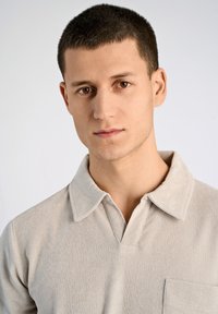 Beżowa bawełniana koszulka polo z kołnierzykiem, kieszenią na lewej piersi oraz miękką, strukturalną powierzchnią.