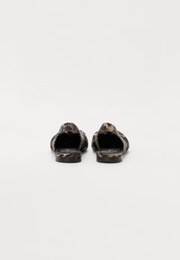 Sandales à enfiler à motif camouflage avec une semelle plate, un dessus en tissu doux et un design à dos ouvert, présentant un léger éclat et un minimum de détails.