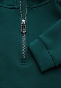 Grüne Zip-Up-Collegejacke mit einem Metall-Reißverschluss, glatter Stoffoberfläche und gerippten Bündchen an den Ärmeln.