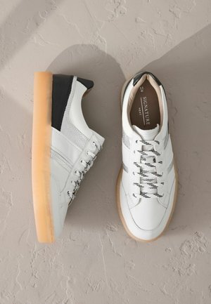 Baskets en cuir blanc avec une finition texturée, talon noir et accents argentés. Elles présentent une semelle en caoutchouc et un design à lacets.