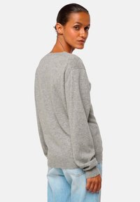 Pull gris surdimensionné en tricot doux avec des manches longues, un col rond et des poignets côtelés, associé à un jean bleu clair.