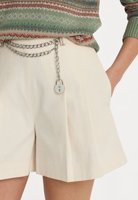Krémové šortky s hladkou strukturou, se stříbrným kovovým páskem a připojeným detailem v podobě zámku.