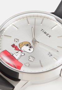 Montre Timex avec un cadran argenté illustré de Snoopy, boîtier en acier inoxydable, bracelet en cuir noir et index horaires traditionnels.