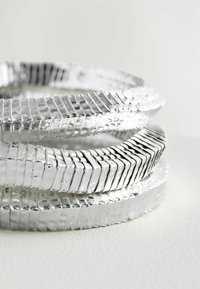 Sæt af tre metaliske sølvarmbånd med en struktureret, ribbet design med varierende tykkelser og glatte overflader.