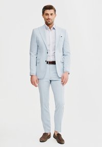 Jasnoniebieski garnitur o slim fit, z klapami w kształcie notcha i jednorzędową marynarką. W komplecie z wzorzystą koszulą i brązowymi butami. W zestawie poszetka.