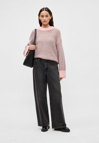 Pulover tricotat cu dungi roz și gri cu mâneci largi, asortat cu blugi negri cu talie înaltă și picioare largi, și pantofi negri, completat de o geantă neagră.