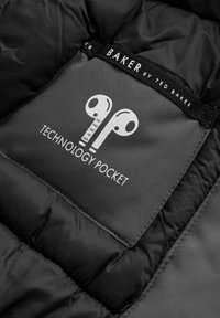 Mustast tikitud sisemusest ja hallist taskust, millel on valge logo. Tekstid on "BAKER" ja "TECHNOLOGY POCKET." Silutud tekstuur.