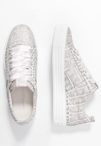 Bílé tenisky s krokodýlím vzorem, vybavené saténovými tkaničkami a tlustou bílou podrážkou. Navrženy pro pohodlí a moderní vzhled.