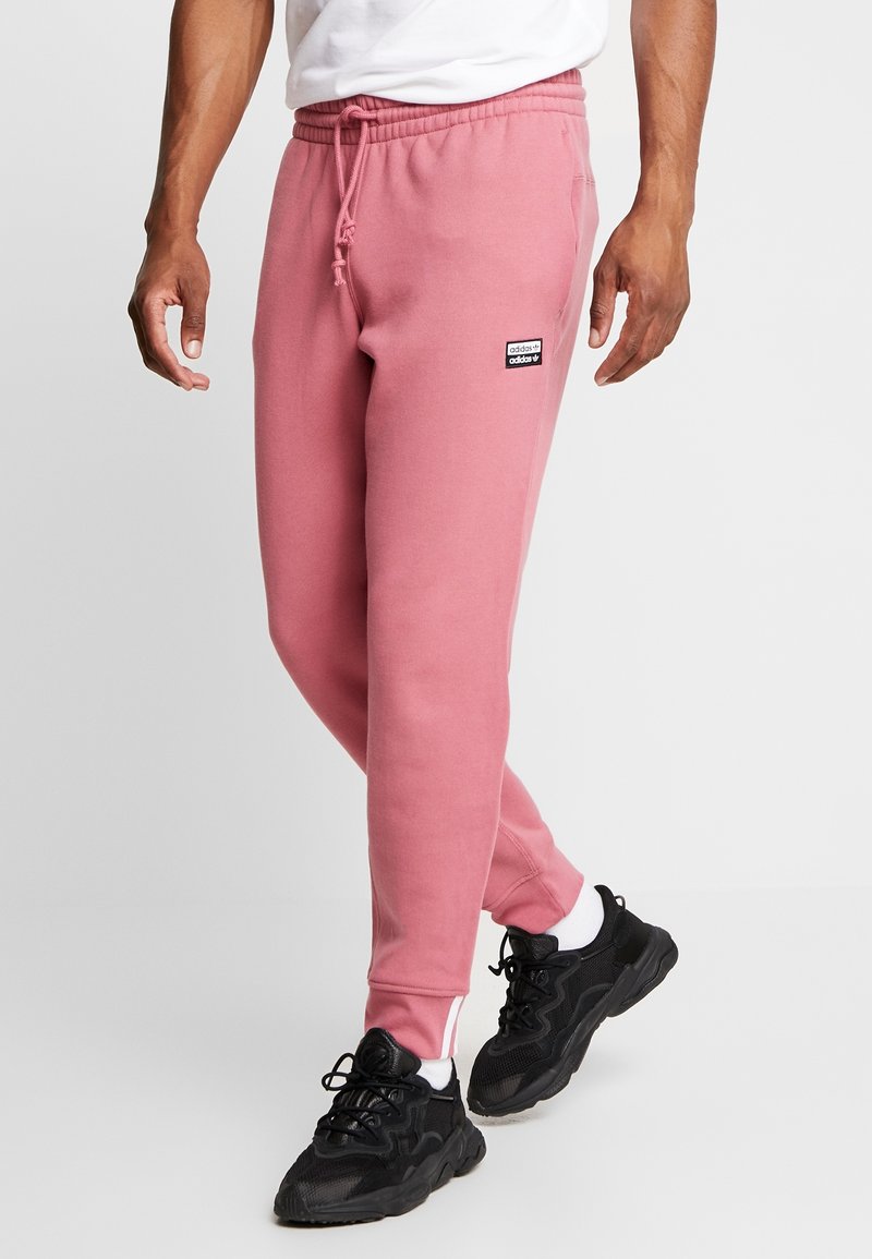 Pink sweatpants made of soft fabric, featuring a drawstring waist, side pockets, and a small black logo patch on the thigh.