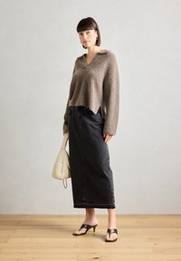 Pull en laine brun, avec un col en V et une longueur cropped. Jupe maxi en denim noir avec des boutons sur le devant. Accompagné d'un sac à main crème et de sandales noires.