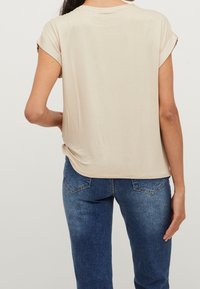 Haut beige à manches courtes avec un col rond et des revers de manches retroussés, associé à un jean en denim bleu avec une coupe classique et des poches latérales.