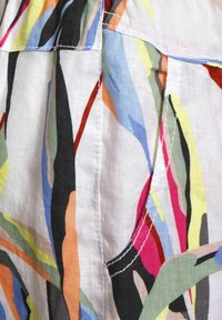 Kangaskudos, jossa on monivärinen abstrakti kuvio, jossa on rohkeat viivat mustana, punaisena, sinisenä, keltaisena ja vihreänä; sisältää taskuyksityiskohtia.