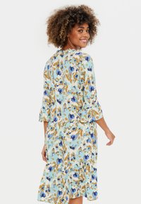 Rochie cu imprimeu floral în bleu deschis, cu accente albastre și aurii, mâneci trei sferturi și design cu partea de jos stratificată; confecționată dintr-un țesătură ușoară.
