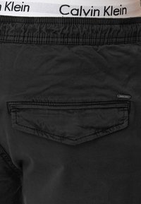 Crne kratke hlače s elastičnom paskom i "Calvin Klein" logom. Imaju stražnji džep s preklopom i šivanim detaljima. Glatka tekstura.