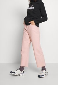 Rosa bomull vida byxor med fransad nederkant, i kombination med en svart sweatshirt och vita sneakers, med en marinblå accent och texturerade strumpor.