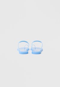 Világoskék papucsok sima, fényes felülettel. Vékony pántokkal és lapos talppal rendelkeznek, alkalmi viseletre tervezve.