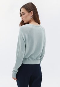 Suéter de punto azul claro con un corte holgado, dobladillo y puños acanalados. Presenta un cuello redondo y un diseño de mangas raglán.