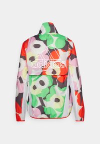 Veste coupe-vent Adidas à motifs floraux colorés avec grand logo Adidas blanc au dos et panneaux de ventilation en mesh sur les côtés.