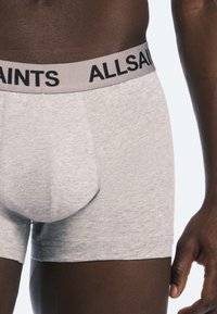 Boxers en coton gris avec un logo "ALLSAINTS" noir sur une ceinture gris clair, présentant un design près du corps. Texture douce.