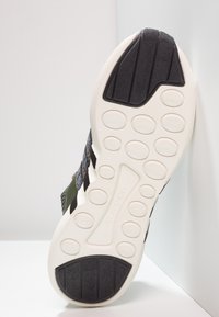 Svart och vit texturerad sula på sneakers med cirkulära mönster och en lätt design. Ovandelen har gröna och svarta meshmaterial.