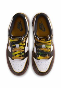 Nike-sneakers har en vit och svart läderöverdel med gula och gröna snören, perforerade detaljer och en brun gummisula.