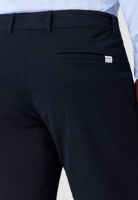 Pantaloni navy con una texture liscia, dotati di una tasca posteriore con zip nascosta e un'etichetta con il marchio. Design attillato.