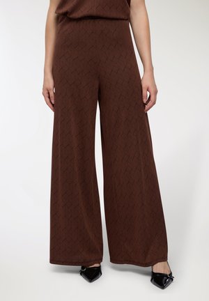 Pantaloni larghi marroni con un motivo geometrico, realizzati in tessuto morbido e con una superficie liscia, abbinati a scarpe nere appuntite.