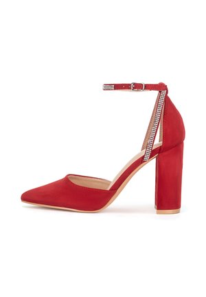 Zapato de tacón alto de ante rojo con punta afilada, correa en el tobillo con detalles de piedras brillantes y tacón grueso de bloque. Textura suave.