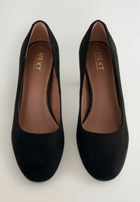 Black suede high-heeled shoes with a rounded toe and a cut-out design on the sides. Interior features brown cushioned insoles.
