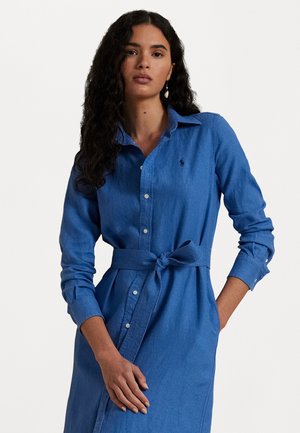 Rochie cămașă din denim de culoare albastru deschis, cu un sistem de închidere cu butoni în față, mâneci lungi, o curea legată în talie și un mic logo pe piept.