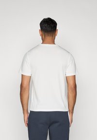 Biela krátka rukávová tričko s okrúhlym výstrihom a hladkou textúrou, zobrazené zozadu, v kombinácii s námorníckymi modrými nohavicami.