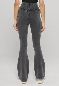 Leggings grises acampanados con una cinturilla alta, que presentan una textura suave y un diseño ajustado. El material parece blando con un ligero estiramiento.