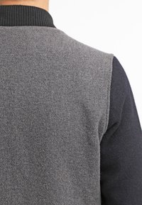 Grijze textielf sweater met een geribbelde zwarte kraag; heeft een geüpdatete, gemêleerde stof op de achterkant en effen donkere mouwen.