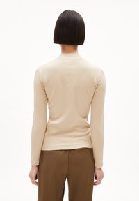 Langärmliges, geripptes T-Shirt in Beige mit rundem Halsausschnitt und nahtlosem Design. Kombiniert mit braunen, hoch taillierten Hosen.