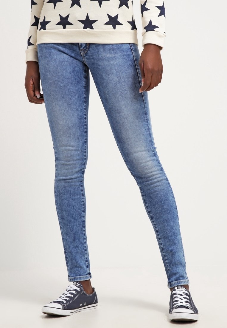 Hellblaue Denim-Skinny-Jeans mit einem ausgebleichten Finish, ausgestattet mit fünf Taschen und einer mittelhohen Taille. Kombiniert mit dunklen Sneakers für einen Kontrast.
