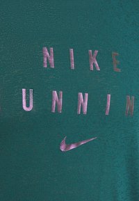 Green athletic shirt with a smooth texture, featuring metallic purple lettering "NIKE RUNNING" and a small Nike logo.