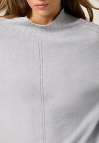 Maglione in grigio chiaro lavorato a maglia con un alto colletto a coste, design senza cuciture sulle spalle e una sottile trama con dettagli di fine cucitura.
