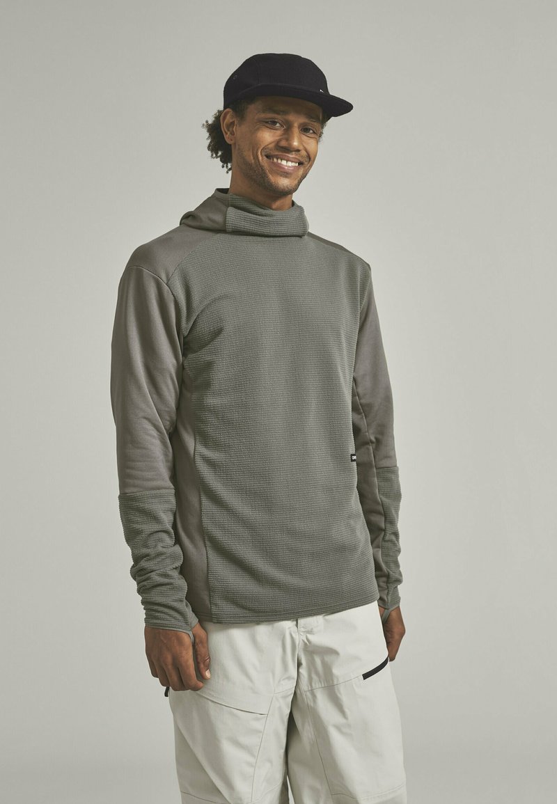 Langärmliger Pullover in Olivgrün mit einer strukturierten Vorderseite, hohem Kragen und kontrastierenden glatten Ärmeln. Passt gut zu Cargohosen.