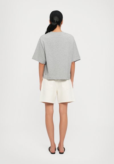 Camiseta gris de manga corta con un ajuste relajado; combinada con pantalones cortos blancos. La camiseta tiene un cuello redondo y una textura suave.