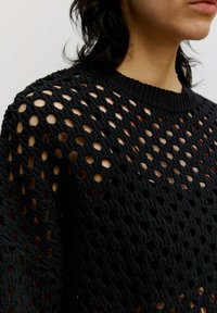 Zwarte gebreide pullover met een breed, open gatpatroon, geribde halslijn en lange mouwen. Gemaakt van textuurgaren.
