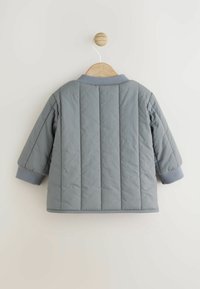 Graue gesteppte Jacke mit rundem Kragen, kurzen Ärmeln und gerippten Bündchen, die auf einem Holzkleiderbügel vor einem schlichten Hintergrund hängt.