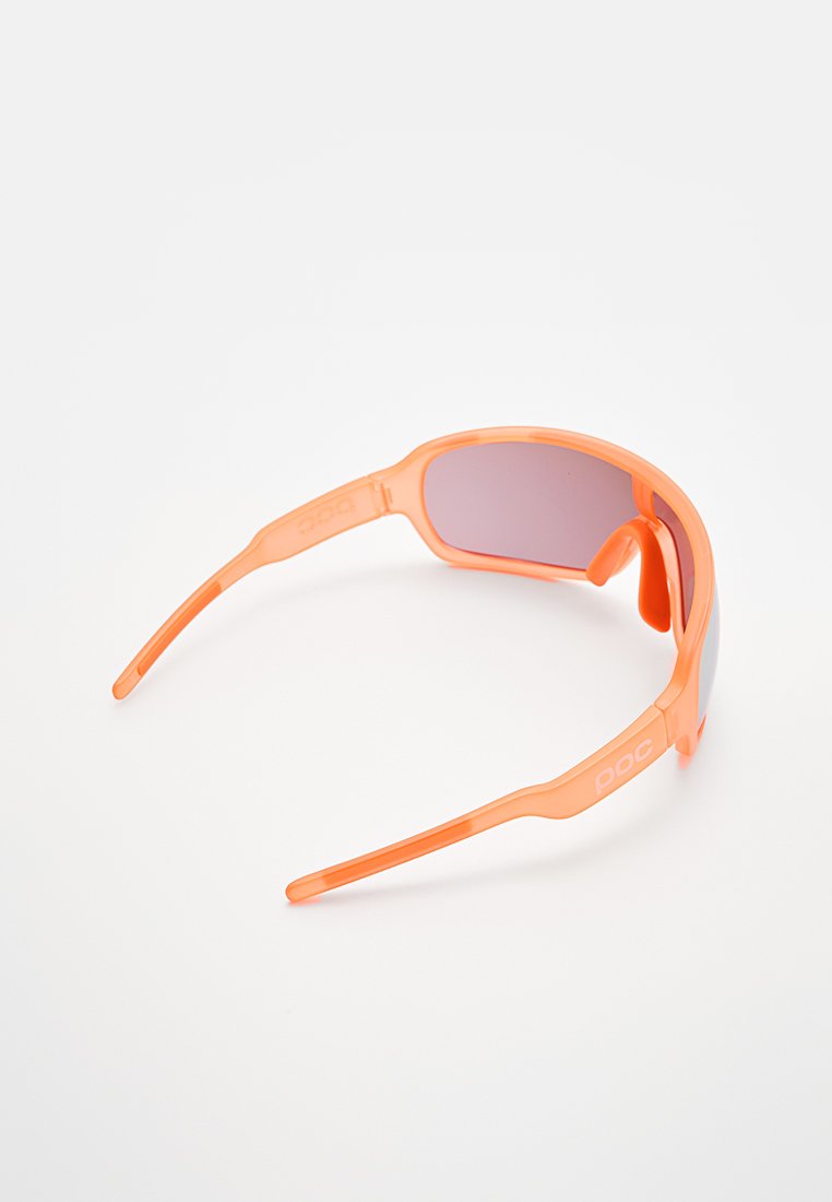 Pomarańczowe przezroczyste okulary przeciwsłoneczne z zakrzywionymi soczewkami, smukłymi ramionami i logo POC. Design cechuje sportowy kształt i gładka faktura.