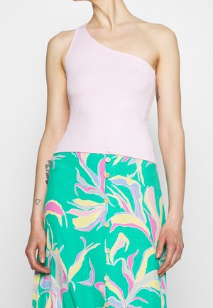 Kvinde iført en lyserød top med ét skulderbånd og et grønt nederdel med knapper med store pastelfarvede blomsterprint.