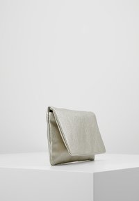 Borsa a pochette metallica argento con una texture liscia, design a pattina piegata e una leggera lucentezza. Forma compatta, appoggiata su una superficie bianca.